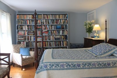 four postered bed in room with wall of books and videos